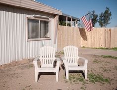 two white lawn chairs sitting in front of a building with an american flag on it