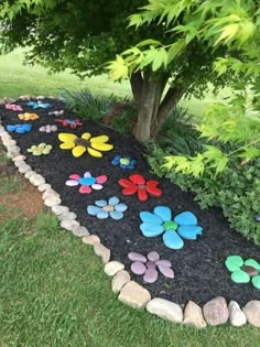 a garden path made out of rocks and stones with colorful flowers on the ground next to a tree