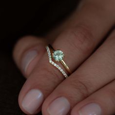 a woman's hand holding a ring with a green stone and diamond on it