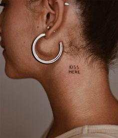 a woman with a small tattoo on her neck and behind her ear that says kiss here