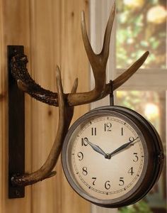 a clock mounted to the side of a wall with antlers on it's face