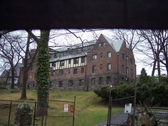 an old brick building with lots of windows on the front and side of it, behind a chain link fence