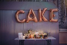 a cake table with candles and balloons on it in front of a metal wall that says cake