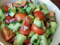 a white bowl filled with cucumber, tomatoes and other vegtables