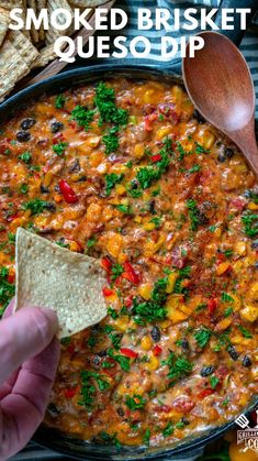 someone is holding a tortilla chip and dipping it into a skillet filled with mexican style quesadilla dip