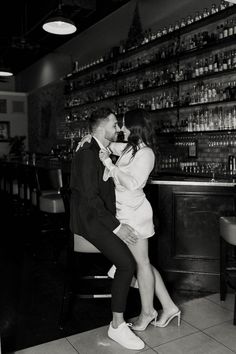 a man and woman kissing in front of a bar with liquor bottles on the wall