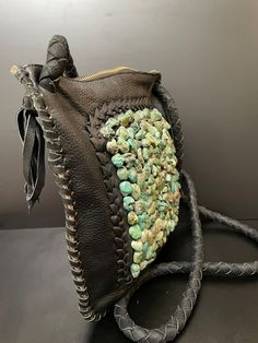 a brown leather purse with green stones on the inside and black braided handle, sitting on a table