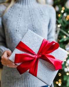 a woman holding a present in front of a christmas tree