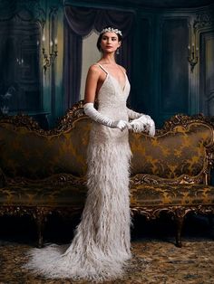 a woman standing in front of a couch wearing a white feathered dress and gloves