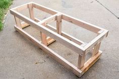 a wooden planter sitting on top of a cement floor next to grass and a sidewalk