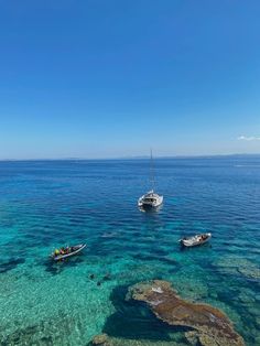 two boats floating on top of the ocean next to rocks and clear blue water in front of a rocky shore