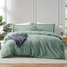 a bed with green sheets and pillows in a room next to a potted plant