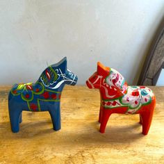 two colorful ceramic dogs sitting on top of a wooden table next to each other in front of a white wall