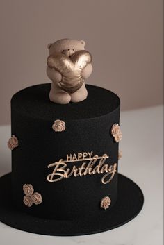 a black birthday cake with a teddy bear on top and happy birthday written on it