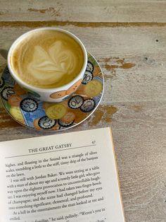 an open book sitting on top of a wooden table next to a cup of coffee