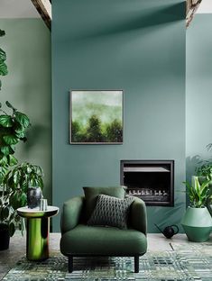 a living room with green walls and a fire place in the corner, surrounded by potted plants