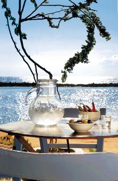 a table with two bowls and a pitcher on it next to the water's edge