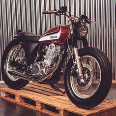 a red and white motorcycle sitting on top of a wooden pallet in front of a metal wall