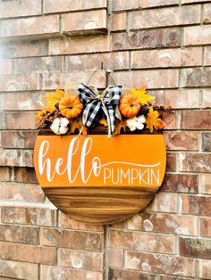 a wooden sign that says hello pumpkin hanging on the side of a brick wall with fall decorations