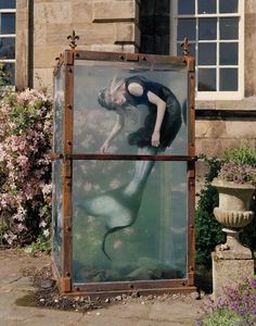 a woman standing in front of a large glass box with a mermaid on it's back