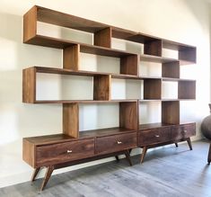 a wooden shelf with two drawers and three shelves on each side, in front of a white wall