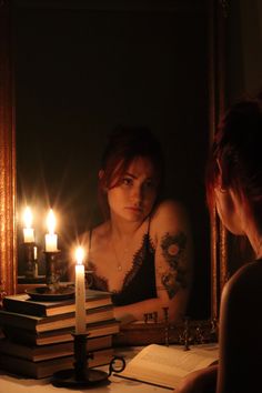 a woman sitting in front of a mirror next to a stack of books with candles