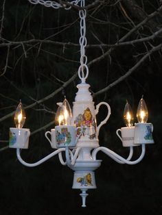 a white chandelier with teacups hanging from it's sides and lit by candles