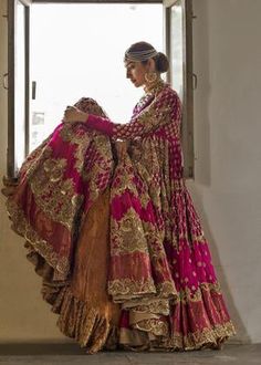 a woman in a red and gold bridal gown standing by a window with her hands on her hips