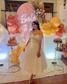 a woman is standing in front of some balloons and cake on the table at a bridal to be party