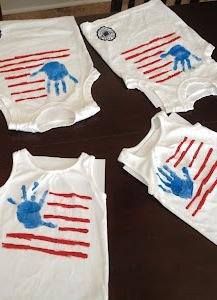 four baby onesuits with handprints on them sitting on a wooden table