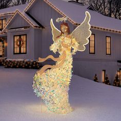 a lighted angel standing in front of a house with christmas lights on it's roof