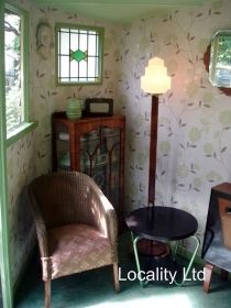 a chair and table in a room with wallpapered walls, windows and a floor lamp