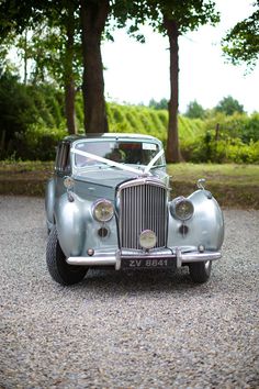 an old car is parked on the gravel