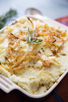 mashed potatoes in a white dish with herbs on top