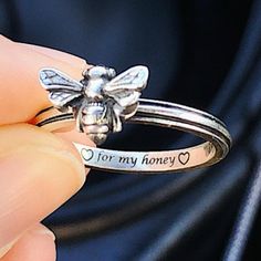 a person holding a silver ring with a bee on it's side and the words for