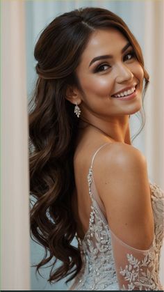 a woman with long dark hair wearing a white dress and smiling at the camera while standing in front of a wall