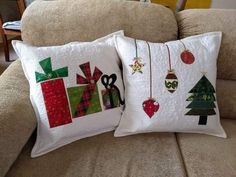 two christmas pillows sitting on top of a couch next to each other with ornaments hanging from them