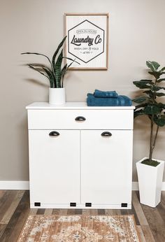 a white cabinet sitting on top of a wooden floor next to a potted plant