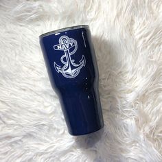 a blue tumbler cup with an anchor on it sitting on a fluffy white surface