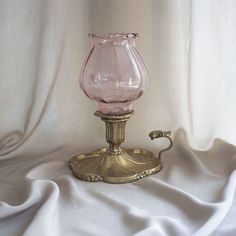 a pink glass vase sitting on top of a metal stand next to a white cloth