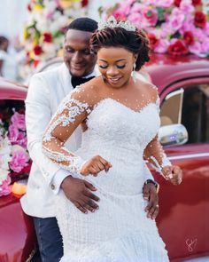 a bride and groom standing next to a red car