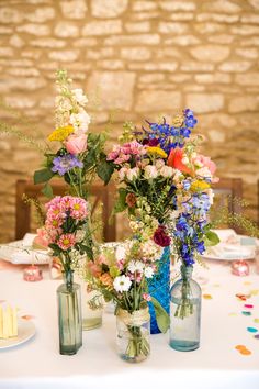 three vases filled with flowers sitting on top of a white tablecloth covered table