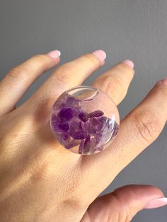 This beautiful ring combines elegance and originality with its unique 27mm glass capsule design. This ring captures the beauty of nature with its liquid filling and amethyst natural stones carefully embedded into the inside of the capsule, adding a subtle yet impactful sparkle. Amethysts is known for its spiritual and calming properties which makes this the best fashion accessory and a symbol of serenity and elegance. The ring band material is designed in transparent resin which allows the capsule and amethyst stones to shine in all their splendor while remaining comfortable and light in your hand. This ring is perfect for special occasions or to add a touch of sophistication to your everyday style. Turn every day into a magical experience by wearing this glass capsule ring with amethyst s Unique Clear Crystal Ring For Gift, Unique Clear Crystal Ring As A Gift, Unique Clear Resin Rings, Unique Clear Resin Ring, Modern Resin Rings For Gifts, Unique Resin Crystal Ring Gift, Clear Crystal Ring Gift, Clear Crystal Ring For Gift, Handmade Clear Rings For Gifts