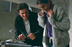 a man and woman standing next to each other in front of a table with items on it