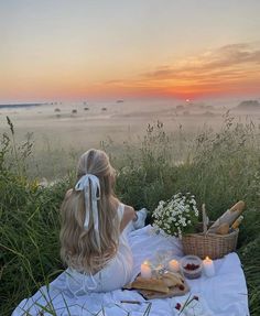 a woman sitting on top of a white blanket next to a basket filled with food