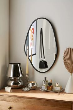 a round mirror on the wall above a dresser with candles and other items in front of it