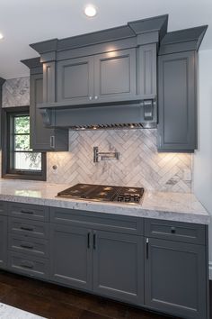 a kitchen with gray cabinets and marble counter tops, along with an oven hood over the stove