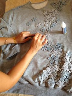 a woman is working on an embroidered t - shirt with flowers and leaves in grey