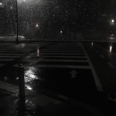 an empty parking lot at night with rain falling on the ground and street lights in the background