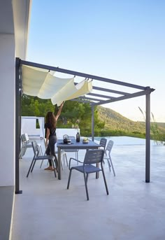 a woman standing under an awning on top of a patio next to a table and chairs